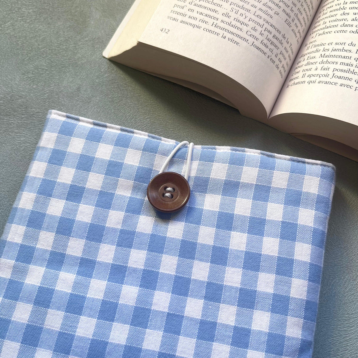 Gros plan sur la fermeture élastique et bouton de récupération en bois brun de la pochette livre tissu vichy bleu clair