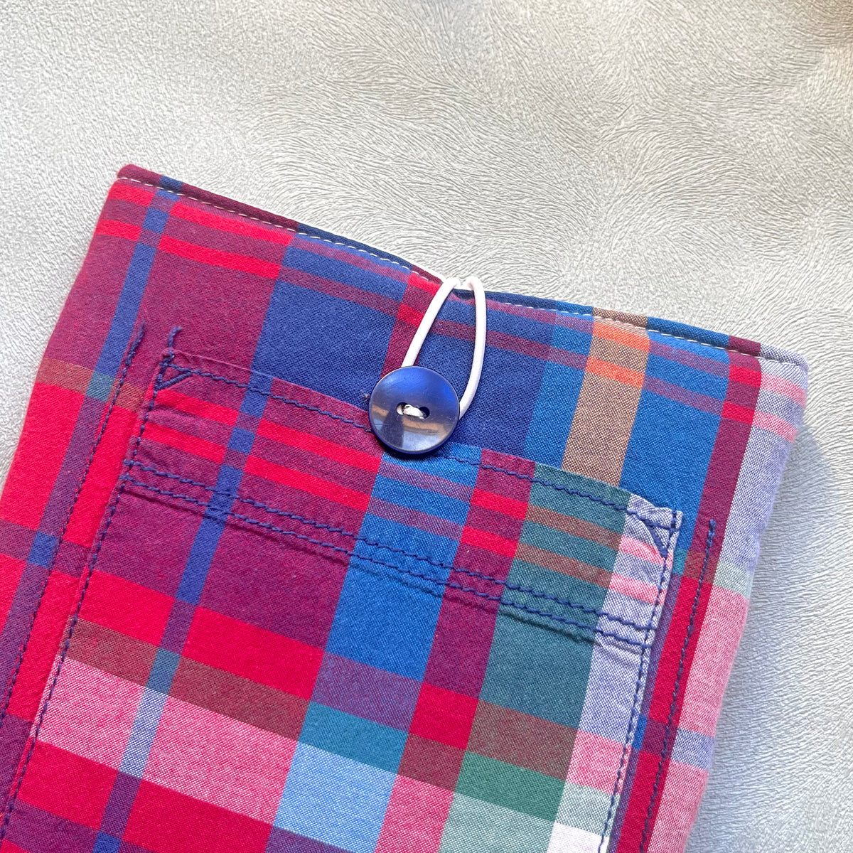 Zoom sur le bouton de récupération bleu marine de la pochette à livre en tissus madras