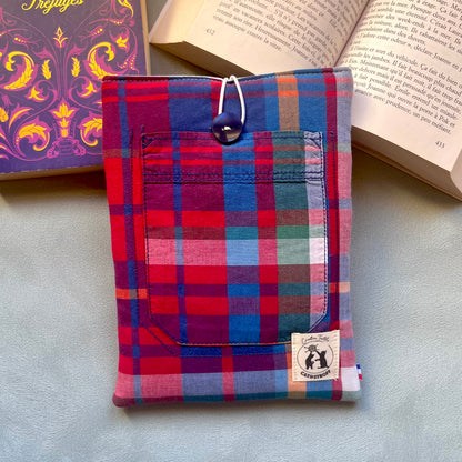 Pochette à livre madras rouge et bleu cousue main, avec poche de chemise et bouton de récupération bleu marine, posée sur un livre ouvert