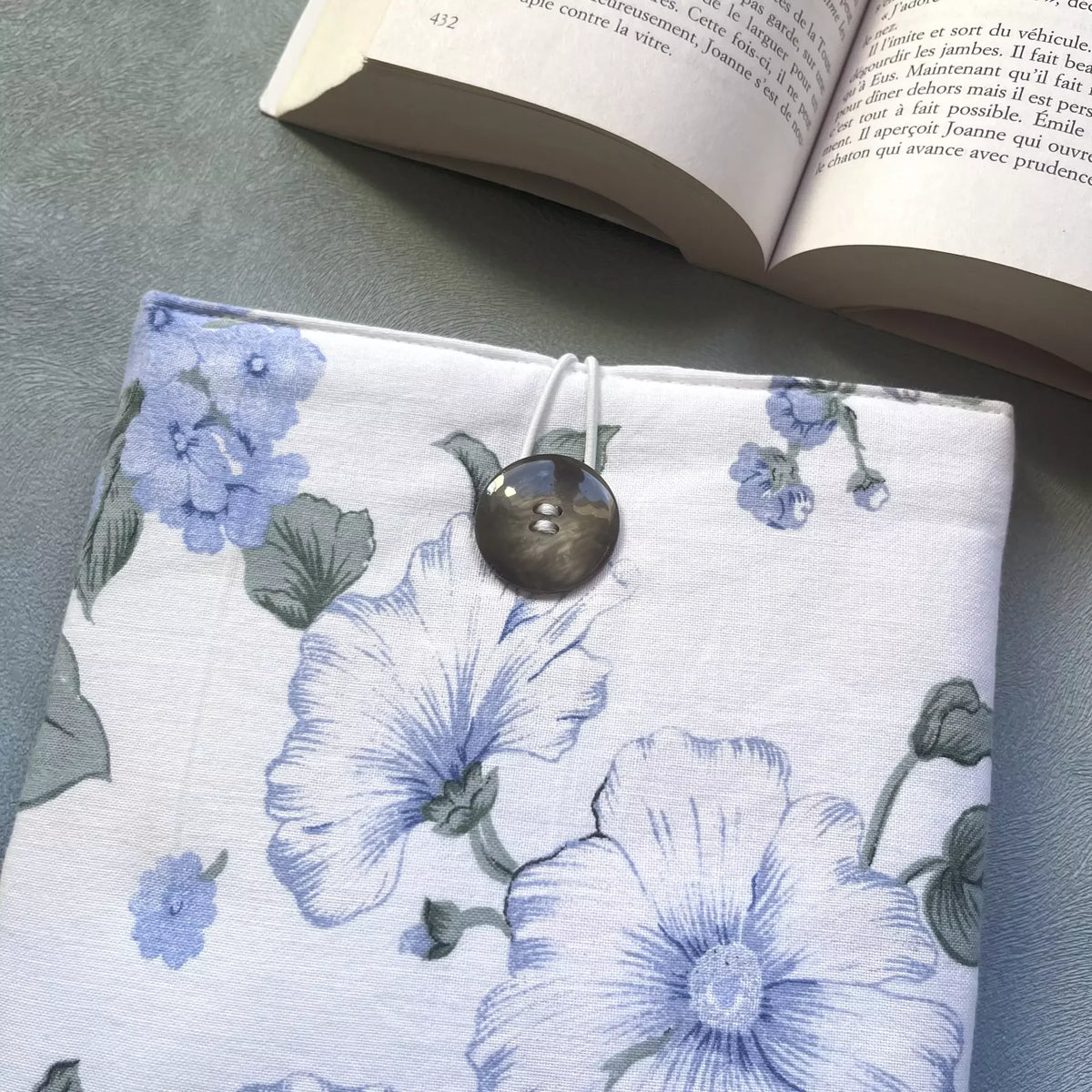 Gros plan sur la fermeture élastique et le bouton de récupération de la housse livre de poche tissu fleuri, détail des grandes fleurs bleues sur fond blanc