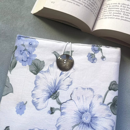 Gros plan sur la fermeture élastique et le bouton de récupération de la housse livre de poche tissu fleuri, détail des grandes fleurs bleues sur fond blanc