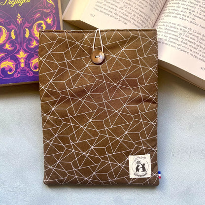 Pochette à livre en coton marron motif géométrique blanc, fermée par un bouton nacré de récupération, posée ici sur un livre ouvert cousue main par Catastroff