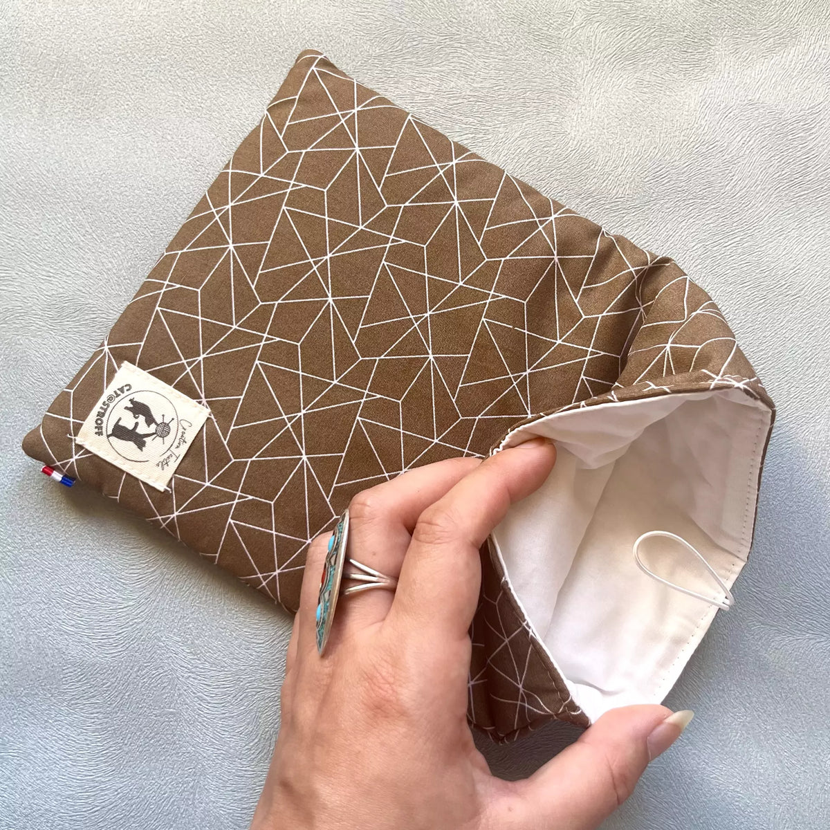 Pochette à livre en coton marron motif géométrique blanc, avec intérieur blanc écru visible sur la photo 