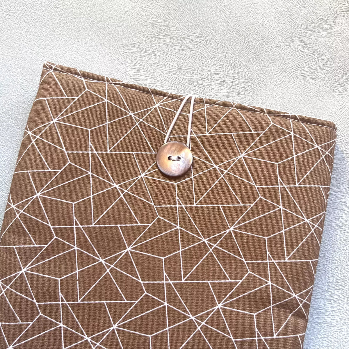 Zoom sur le bouton de récupération nacré de la pochette à livre en coton marron motif géométrique