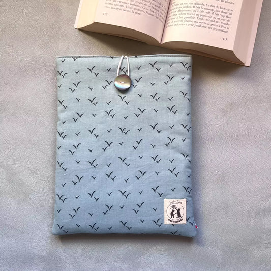 Pochette à livre bleu oiseau Envolée Bleue vue de face posée à plat, motif oiseaux en vol sur coton bleu ciel, étiquette Catastroff visible