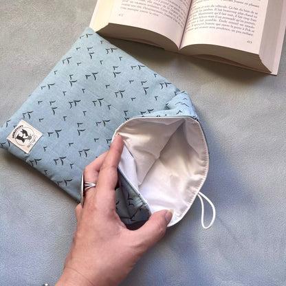 Pochette livre tissu molletonné Envolée Bleue ouverte par une main, doublure intérieure claire blanche visible, label Catastroff sur le côté
