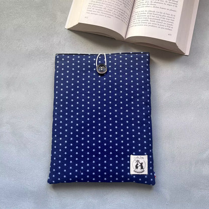 Pochette à livre bleu etoilé La Belle Étoile posée à plat, motif étoiles claires sur fond bleu nuit, bouton de récupération visible, livre ouvert en arrière-plan.