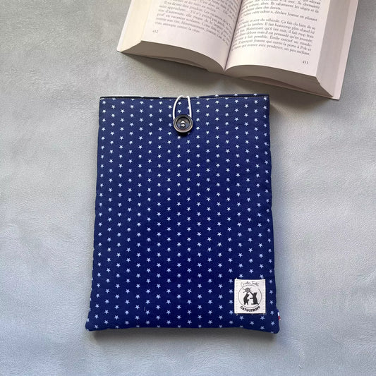 Pochette à livre bleu etoilé La Belle Étoile posée à plat, motif étoiles claires sur fond bleu nuit, bouton de récupération visible, livre ouvert en arrière-plan.