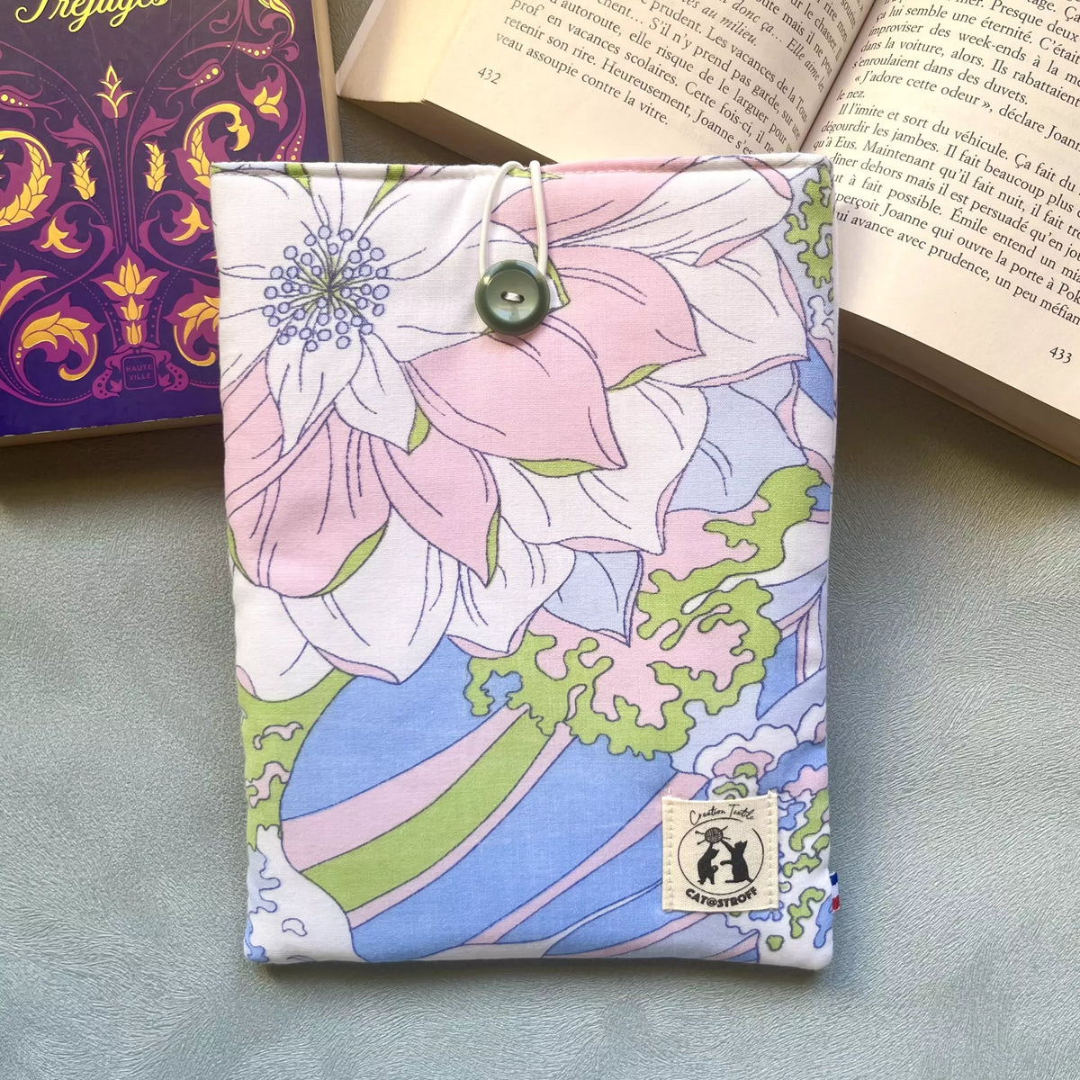 Pochette à livre en coton fleuri pastel upcyclé avec bouton de récupération vert, ici posé sur un livre ouvert