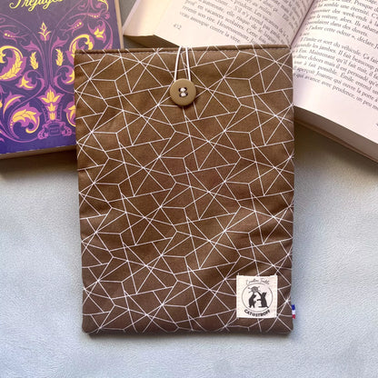 Housse livre poche voyage tissu Puzzle Café posée à plat entre deux livres ouverts, motif géométrique brun et blanc, étiquette Catastroff visible.