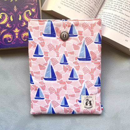 Pochette à livre tissu coton imprimé voiliers bleus et traits roses, cousue main, fermée par un bouton récupéré et posé sur un livre ouvert 