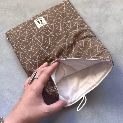 Pochette à livre grand format Cacao Graphique ouverte, doublure claire visible, tenue en main pour montrer la profondeur et le molleton intérieur