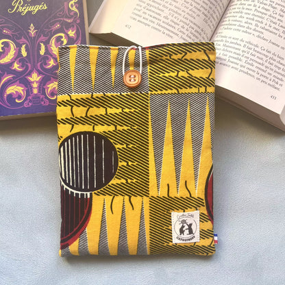 Pochette livre de poche en tissu wax africain jaune et noir avec bouton caramel, ici posée sur un livre ouvert, faite main par Catastroff