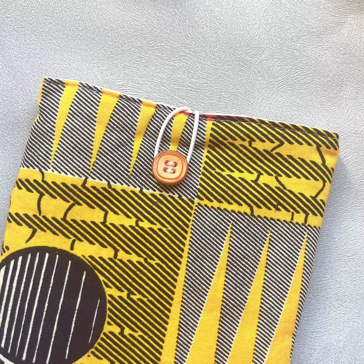 Zoom sur le bouton de récupération caramel, de la pochette livre de poche en tissu wax africain jaune et noir, faite main par Catastroff