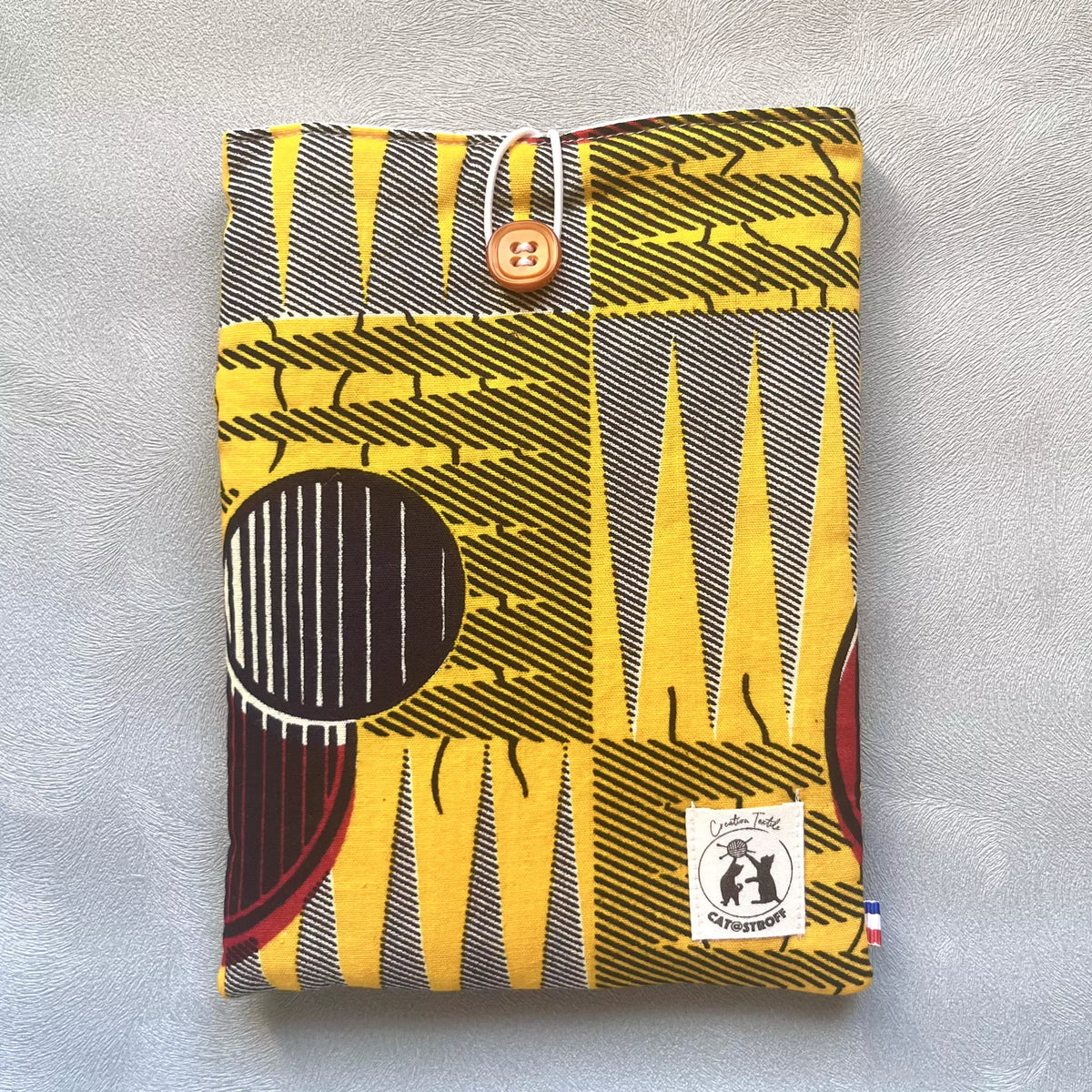 Pochette livre de poche en tissu wax africain jaune et noir avec bouton caramel, faite main par Catastroff
