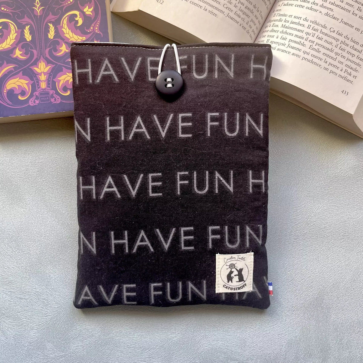 Pochette à livre upcyclés noir motif Have Fun, cousue main, vue recto avec bouton de récupération et posé sur un livre ouvert